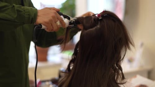 Male hairdresser ironing a woman's hair