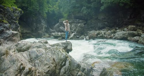Woman enjoys the view on rocky bank near a fast flowing powerful deep mountain river. Nature landsca