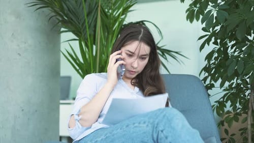 Young Woman Talking on Phone Examining Documents Indoors
