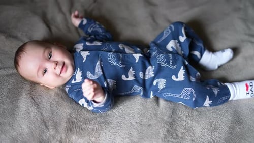 Sweet healthy toddler boy in blue clothes lies on bed. Adorable boy looking into camera