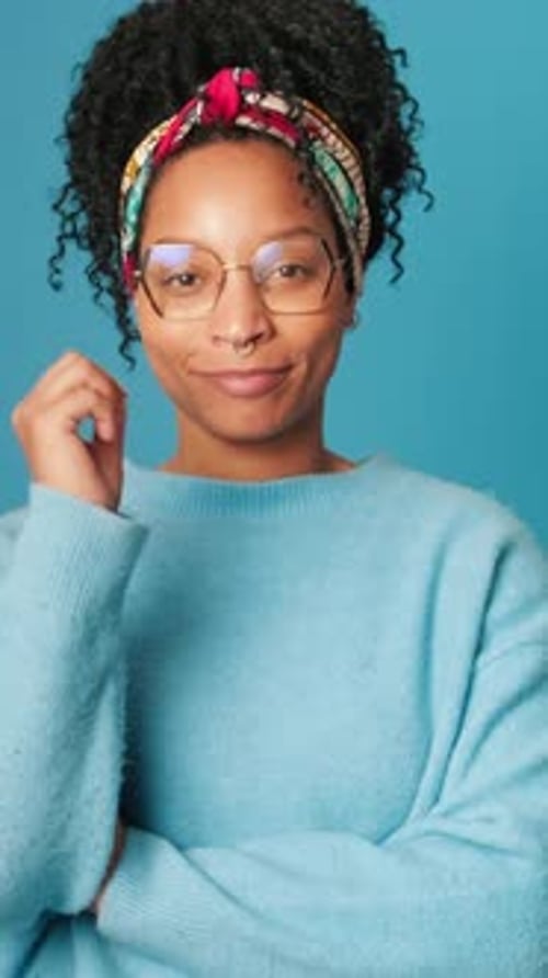 Smiling young woman showing thumbs up and looking at camera on blue background in studio