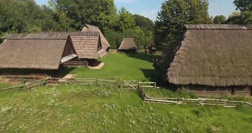 Alte Holzhütten in einem malerischen Freilichtmuseum, im Sommer von Bäumen umgeben. Dynamische Drohne s