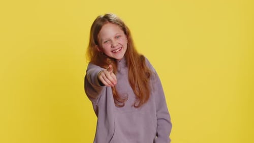 Smiling Girl Points to Camera on Yellow Background