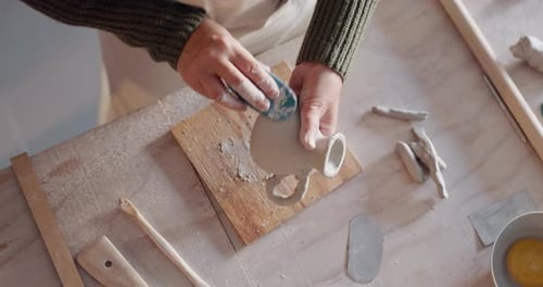 Craftsperson Shaping Clay Vessel on Workbench