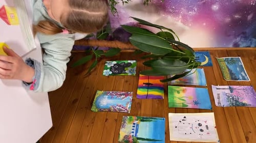 Child Drawing at Desk with Artworks on Floor