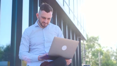 Smart Businessman Using Laptop in Urban Environment Sitting in Front of Office Building During Break