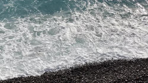 Azurblaues Wasser schlägt an einem Kiesstrand bei Sonnenuntergang Meer Schaum Sonnenreflexionen auf dem Wasser Keine Seele