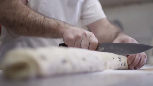 Nahaufnahme der Hände eines Mannes, der in der Küche einer Bäckerei eine Rolle Fruchtteig schneidet