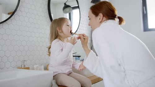 Woman helping young girl brush teeth in bathroom