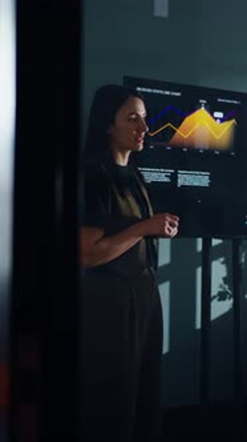 Confident Businesswoman Presenting Analytics Data on Large Screen with Colorful Line Charts During