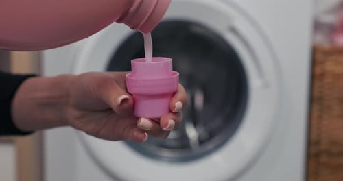 Laundry Detergent Being Poured into Pink Cap