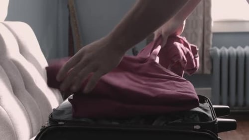 Person Packing Clothes in Suitcase at Home