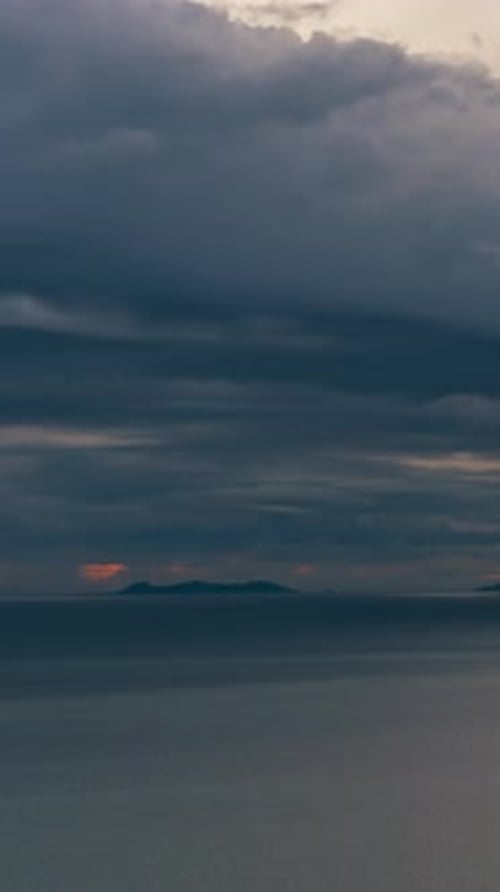 Vidéo verticale. Soleil éclatant et nuages épais au-dessus d'un océan tranquille avec des îles illuminées au loin