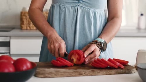 Woman Slices Tomatoes on a Cutting Board in Kitchen