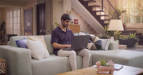 Un homme hindou concentré tape sur un ordinateur portable, fait du travail à distance dans un bureau à domicile confortable, complète une communication électronique