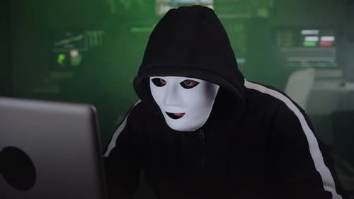 Masked Hacker in Dark Room Typing on Laptop