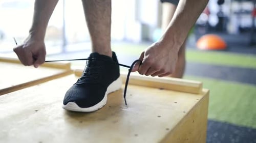 Feet of Young Man Tying Shoelaces on His Sport Shoe in Gym
