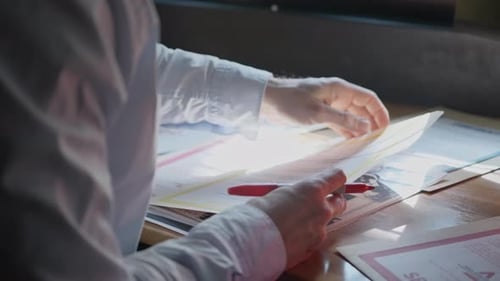 Gros plan des mains à un bureau feuilletant des papiers et des dossiers confidentiels, marquant les détails clés