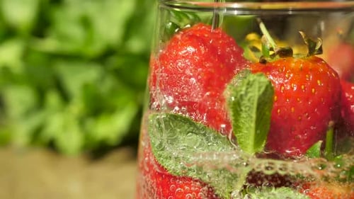 Closeup of Pouring Soda Into a Glass with Fresh Strawberries and Green Mint Leaves in Slow Motion