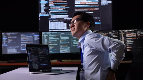 Programmer Having A Backache While Writing Code By A Laptop Using Multiple Monitors Showing Database