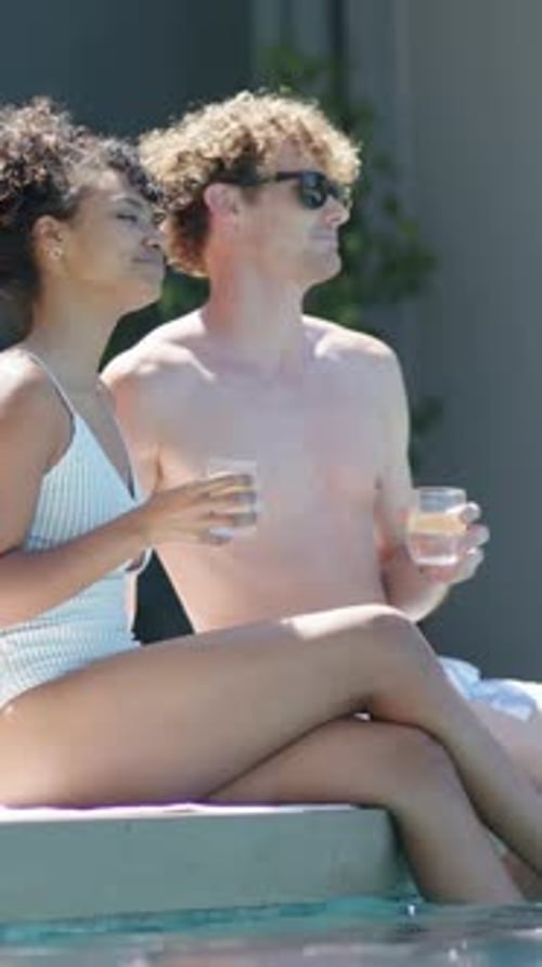 Vertical video: Sunlight urging couple wearing swimwear and sunglasses, sipping drinks at pool deck