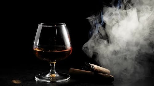 Glass of Liquor with Smoking Cigar on Black
