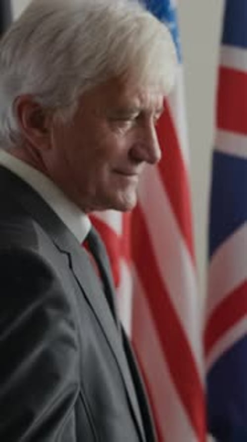 Man in Suit Speaking with Flags Behind