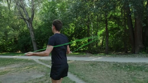 A simple yet effective way to stay healthy: a man exercises with a jump rope outdoors in a green par