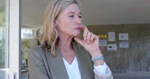 Thinking deeply, senior woman in casual attire with hand on chin indoors, in office