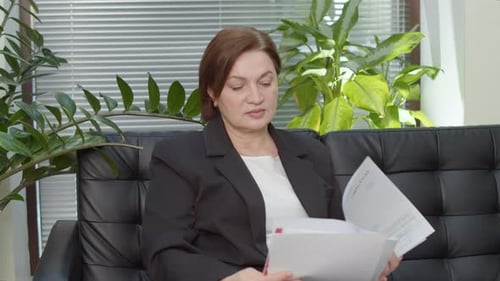 Businesswoman Studying Report on Black Sofa in Office