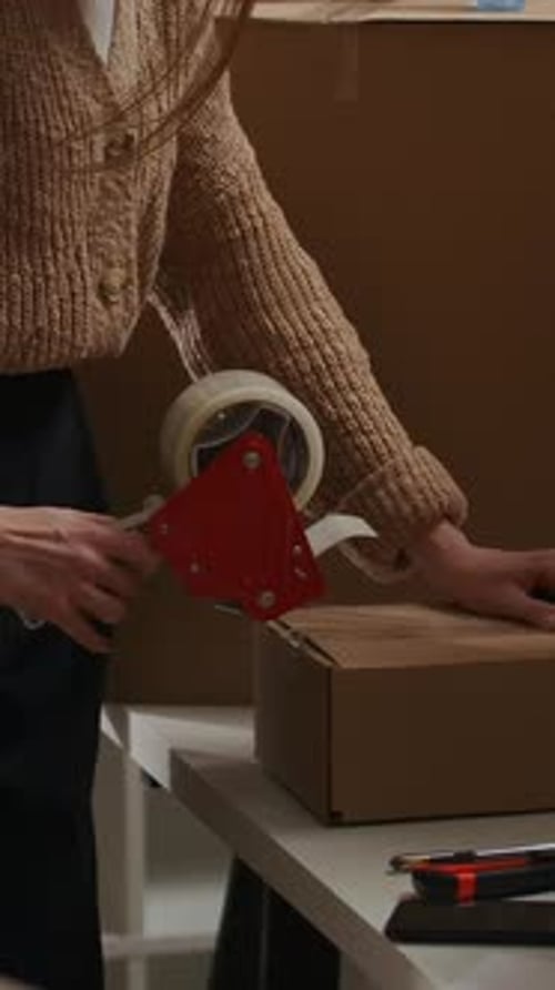 Woman Sealing Cardboard Box with Tape Gun in Home