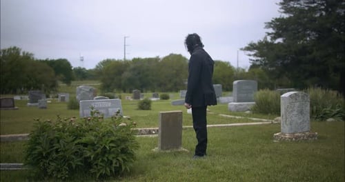 Man in black suit in cemetery for funeral ceremony.