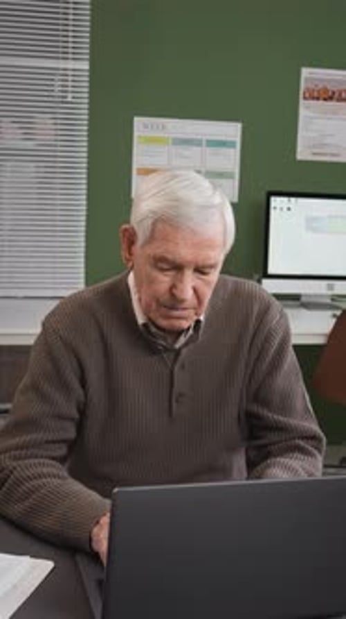 Vertical of Senior Man Looking at Camera by Laptop in Computer Class
