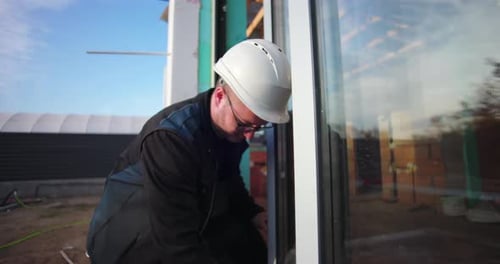Worker in hard hat inspecting window frame alignment on building site, focusing on accuracy and