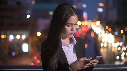 A young beautiful business woman is using smart phone in city over traffic lights