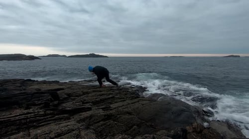 Männlicher Erwachsener sitzt auf einem Felsen in der Nähe des Meeres und benutzt sein Handy, bevor er aufsteht und weggeht -