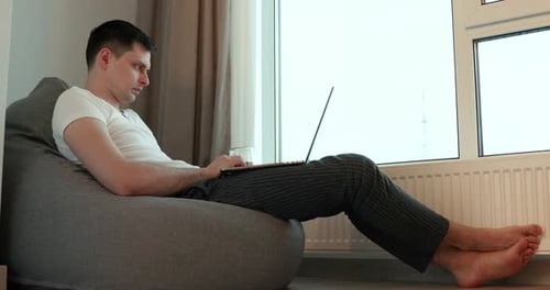 Man Relaxing at Home Using Laptop on Beanbag