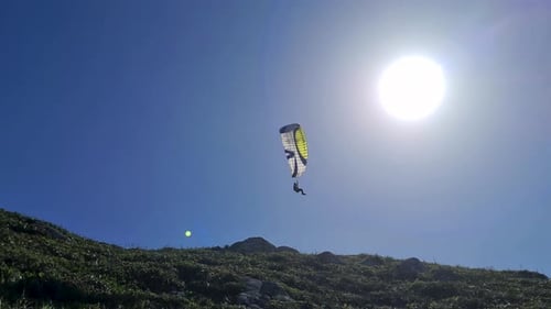 Scene of person flying a paraglider near mountains with lots of vegetation and blue sky air sports o