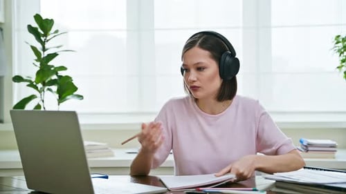 Young Female College Student in Headphones Studying Using Laptop Computer for Video Chat