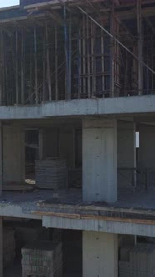 Vídeo vertical: vista aérea de trabajadores manipulando hormigón, metal y planos en una construcción bulliciosa