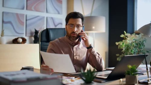 Serious Confident Businessman Calling at Office Desk Looking Work Papers. Middle-Aged Bearded