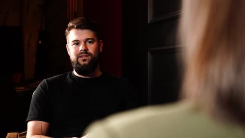 Blick über die weibliche Schulter auf den Mann mit Bart beim Studiointerview im Innenbereich