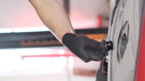 Close Up Automotive Mechanic Inserts Something into Wheel
