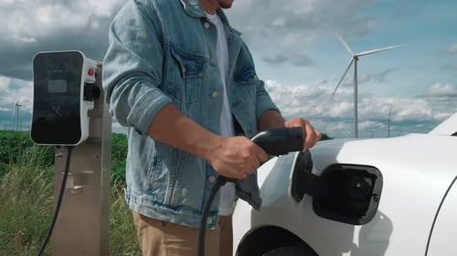 Progressive Man with His EV Car and Wind Turbine As Concept of Renewable Energy