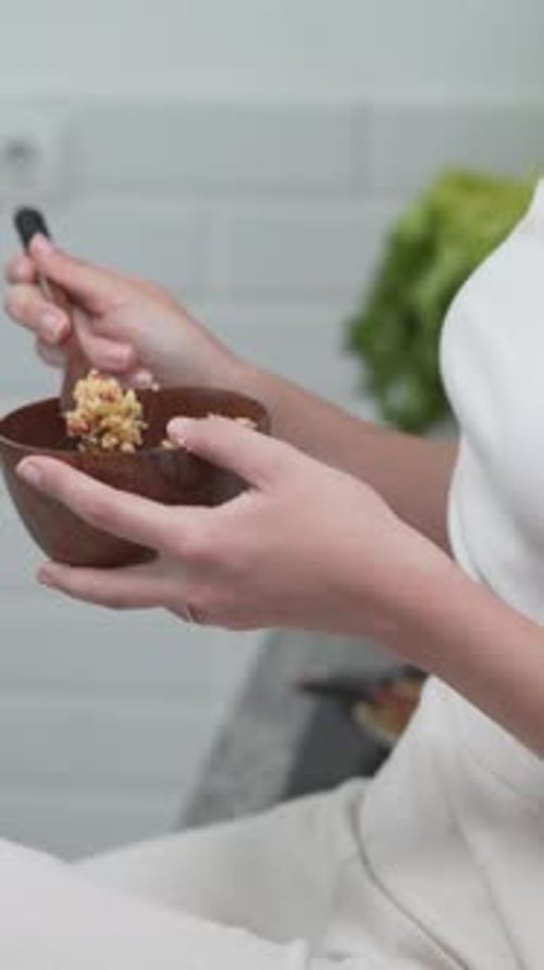 Woman Eats from Wooden Bowl with a Spoon