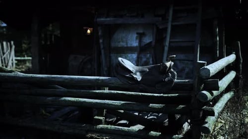 Saddle Resting on a Rustic Wooden Fence at an Old Barn During Twilight