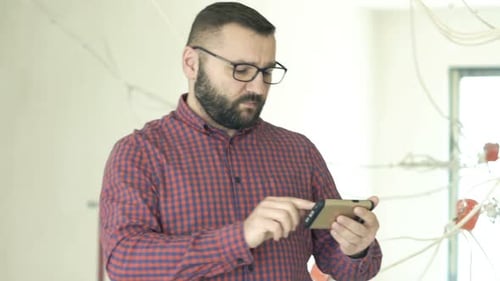 Man with beard uses smartphone in bare interior