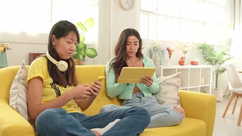 Young Women Relaxing Together on Sofa with Tech