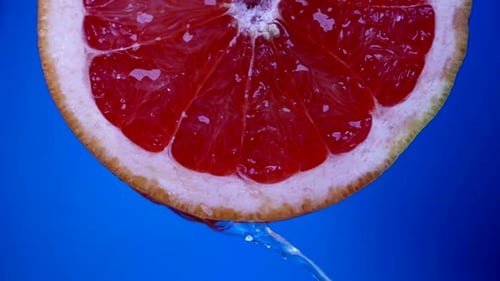 Juicy Grapefruit Half with Water on Blue Background