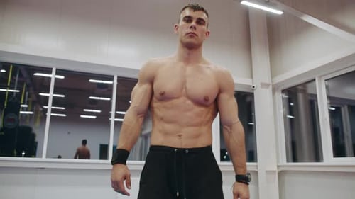 A Young Muscular Man with a Naked Torso Goes Through the Gym and Kneads His Hands Clasping Them in a